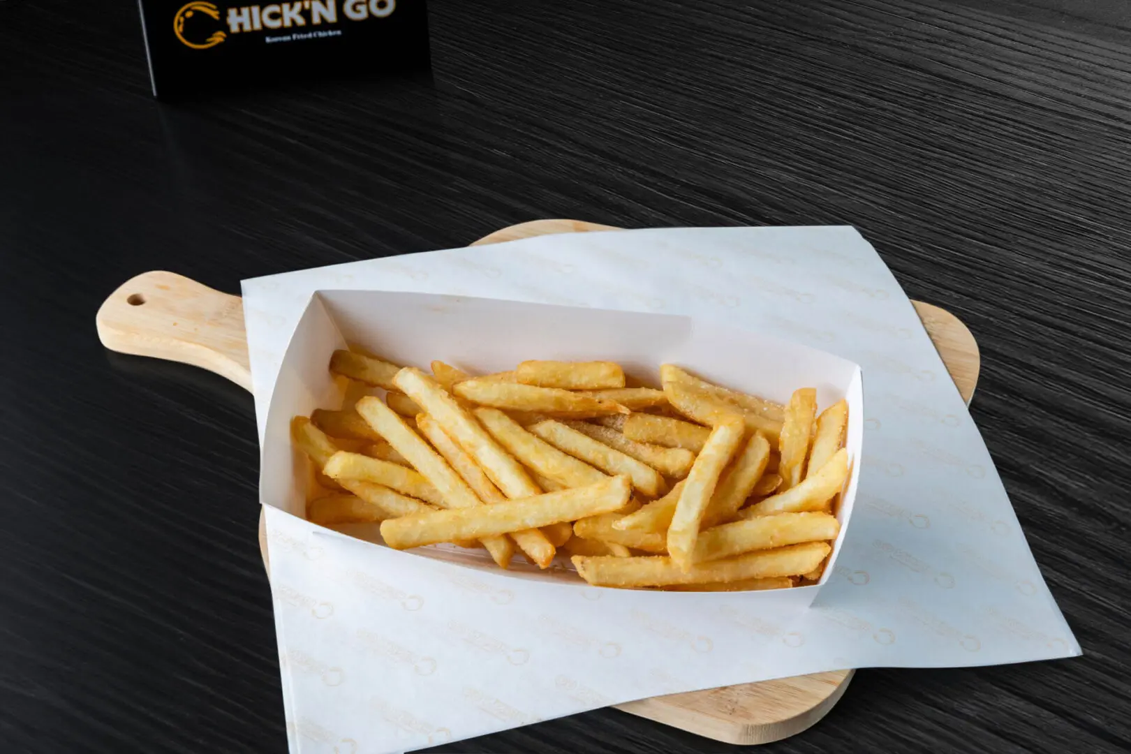 A box of fries on top of a wooden board.